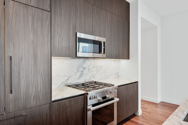 kitchen with backsplash, appliances with stainless steel finishes, light stone counters, and light hardwood / wood-style flooring