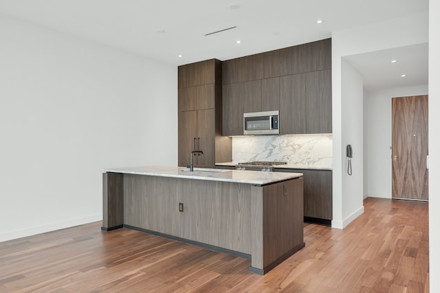 kitchen with stainless steel appliances, sink, tasteful backsplash, a kitchen island with sink, and light wood-type flooring