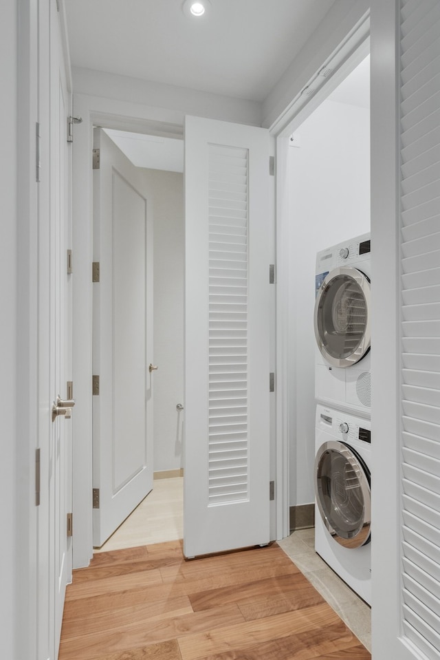 clothes washing area featuring stacked washer and clothes dryer and light hardwood / wood-style flooring