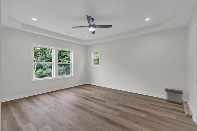 empty room featuring a tray ceiling, ceiling fan, and light hardwood / wood-style flooring