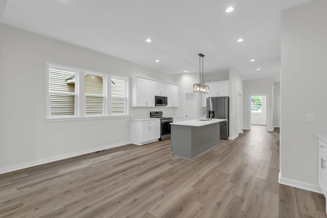 kitchen with stainless steel appliances, light hardwood / wood-style floors, a center island with sink, white cabinetry, and pendant lighting