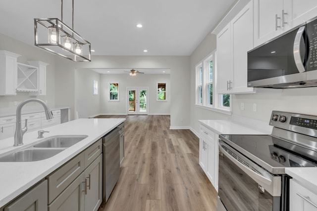 kitchen with sink, pendant lighting, light wood-type flooring, appliances with stainless steel finishes, and white cabinetry