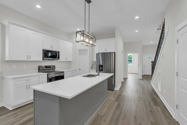 kitchen with a center island with sink, sink, pendant lighting, appliances with stainless steel finishes, and white cabinetry