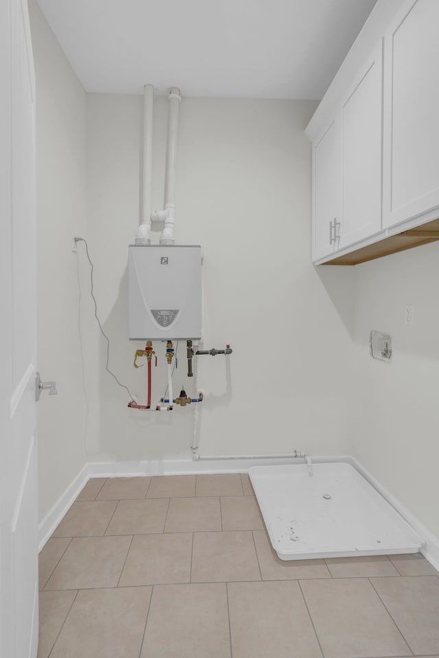 clothes washing area with cabinets, tankless water heater, and light tile patterned floors