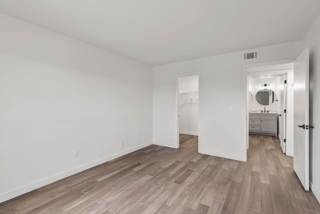 unfurnished bedroom with a walk in closet, a closet, light hardwood / wood-style floors, and sink