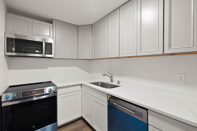 kitchen with sink, dark wood-type flooring, stainless steel appliances, light stone counters, and white cabinets