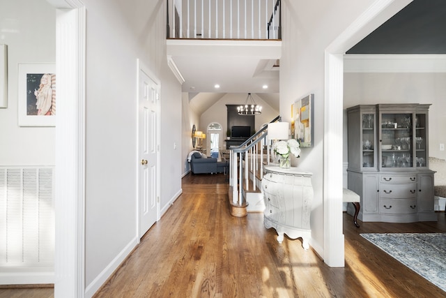 hall with a high ceiling, a notable chandelier, hardwood / wood-style flooring, and crown molding