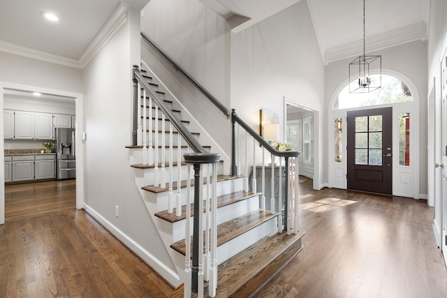 foyer entrance with a towering ceiling, dark hardwood / wood-style floors, an inviting chandelier, and crown molding