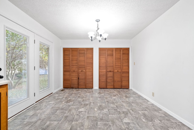 unfurnished bedroom featuring access to exterior, a textured ceiling, an inviting chandelier, and two closets