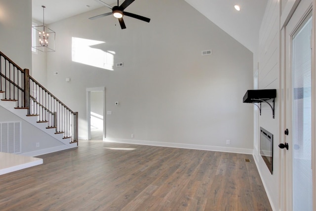 unfurnished living room featuring a high ceiling, ceiling fan with notable chandelier, and hardwood / wood-style floors