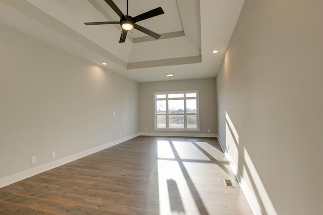 unfurnished room featuring hardwood / wood-style flooring, a raised ceiling, a towering ceiling, and ceiling fan