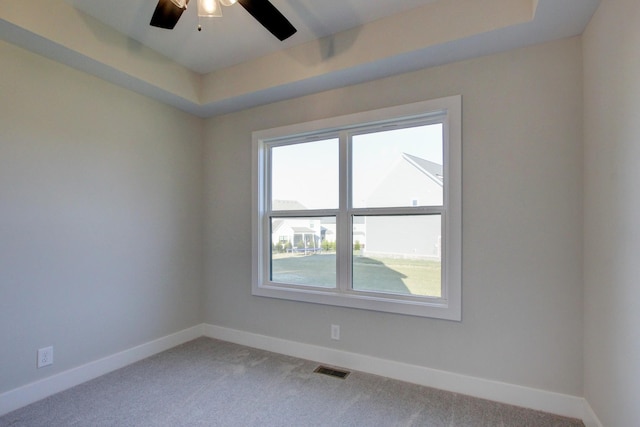 empty room featuring carpet floors, a tray ceiling, plenty of natural light, and ceiling fan