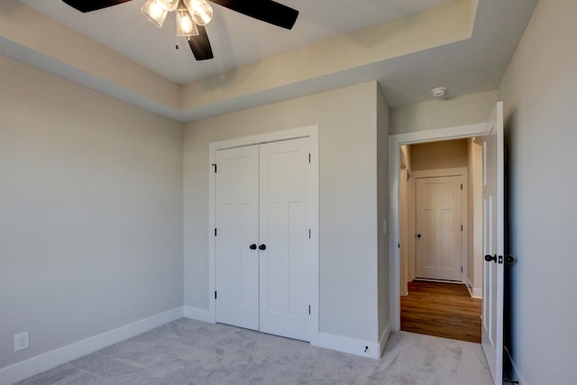 unfurnished bedroom featuring a raised ceiling, light carpet, ceiling fan, and a closet