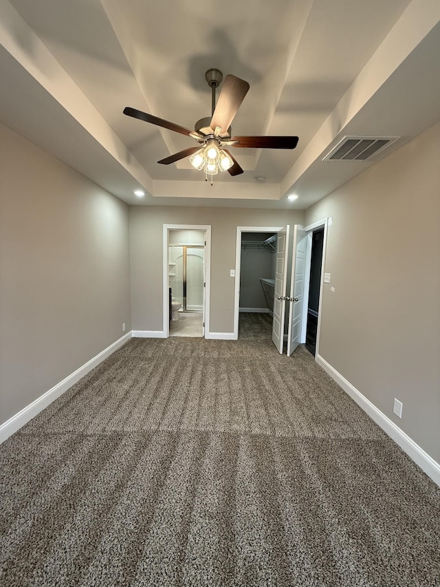 unfurnished bedroom featuring ceiling fan, ensuite bathroom, carpet floors, a raised ceiling, and a closet