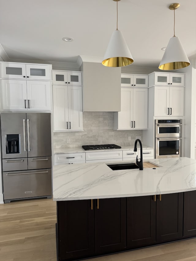 kitchen with stainless steel appliances, sink, a large island with sink, decorative light fixtures, and white cabinets