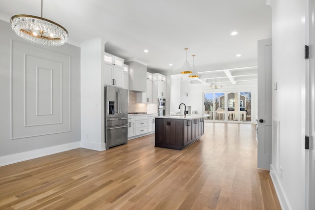 kitchen with light wood finished floors, light countertops, appliances with stainless steel finishes, a sink, and a chandelier