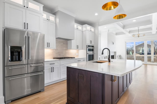 kitchen featuring coffered ceiling, a sink, appliances with stainless steel finishes, light wood finished floors, and tasteful backsplash