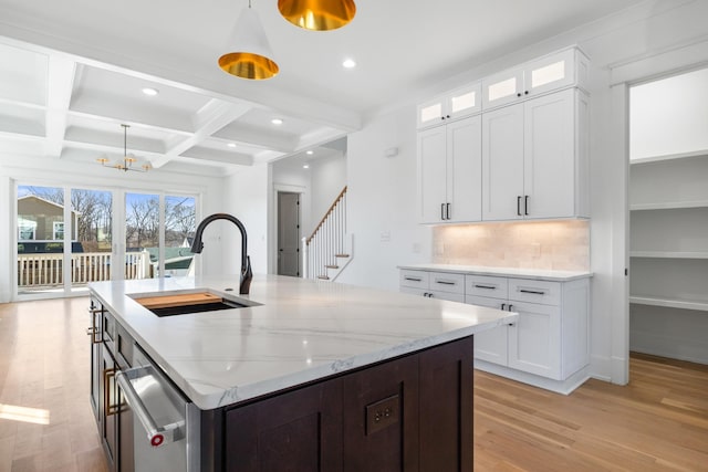 kitchen with light stone counters, a sink, light wood-type flooring, coffered ceiling, and beamed ceiling