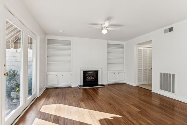 unfurnished living room with built in shelves, dark wood-type flooring, a healthy amount of sunlight, and ceiling fan