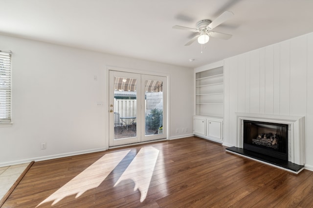 unfurnished living room featuring built in shelves, dark wood-type flooring, and ceiling fan