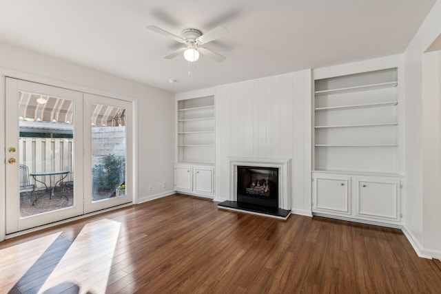 unfurnished living room featuring built in shelves, a large fireplace, dark hardwood / wood-style floors, and ceiling fan