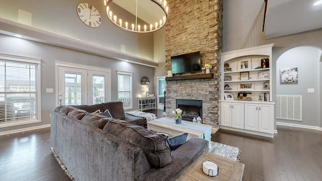 living room with built in features, a high ceiling, a notable chandelier, dark hardwood / wood-style flooring, and a stone fireplace