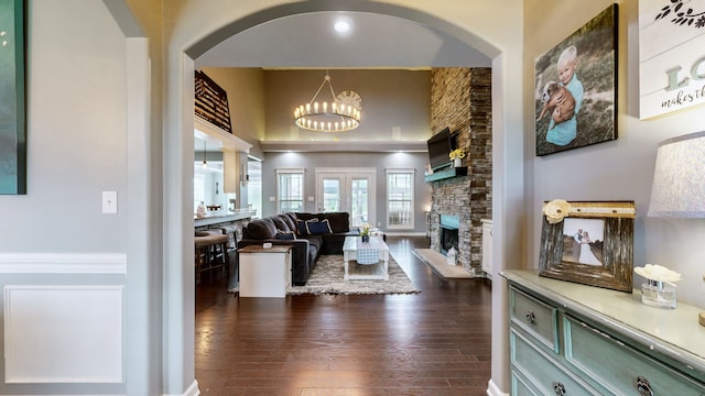 living room with dark hardwood / wood-style flooring, a chandelier, a stone fireplace, and a high ceiling