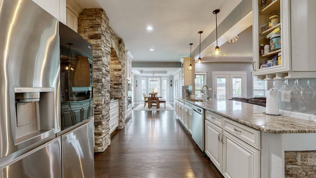 kitchen with dark wood-type flooring, light stone counters, hanging light fixtures, appliances with stainless steel finishes, and white cabinets