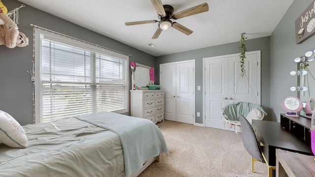 carpeted bedroom with ceiling fan and two closets