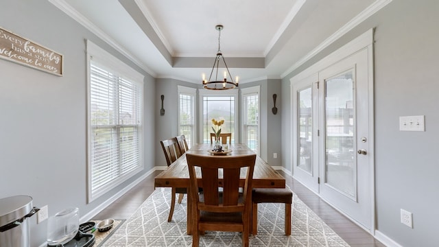 dining space with a chandelier, ornamental molding, a raised ceiling, and light wood-type flooring