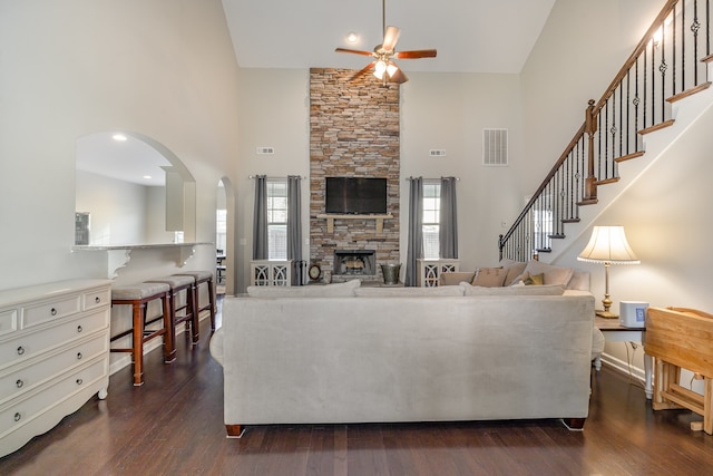 living room featuring dark hardwood / wood-style floors, ceiling fan, a stone fireplace, and high vaulted ceiling