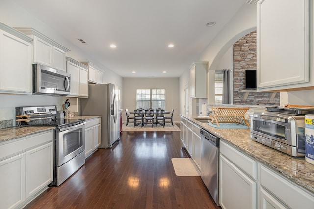 kitchen featuring light stone countertops, appliances with stainless steel finishes, white cabinetry, and dark wood-type flooring