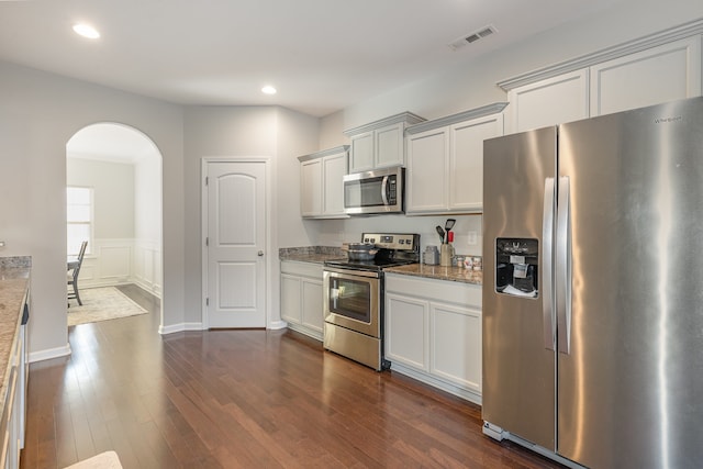 kitchen with light stone countertops, stainless steel appliances, white cabinets, and dark wood-type flooring