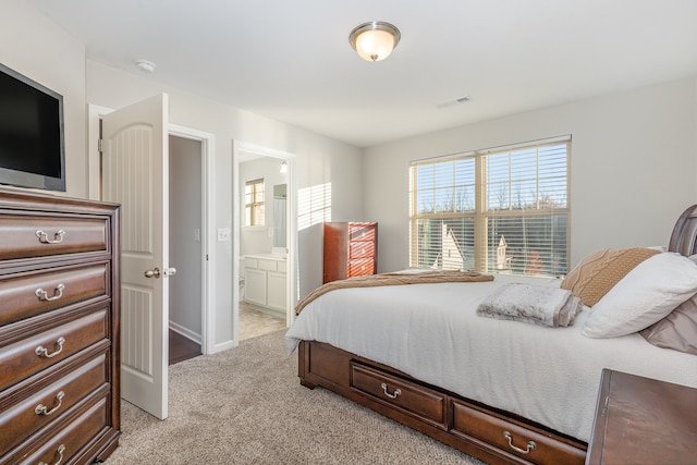 bedroom with ensuite bathroom and light carpet