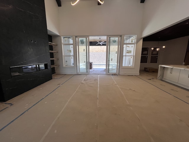 unfurnished living room featuring a tiled fireplace, built in features, ceiling fan, and a high ceiling