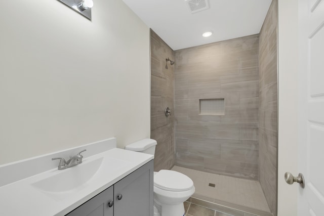 bathroom with a tile shower, vanity, tile patterned floors, and toilet