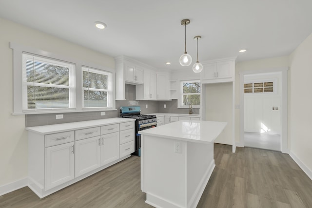 kitchen with gas range, a kitchen island, white cabinetry, light wood-type flooring, and decorative light fixtures