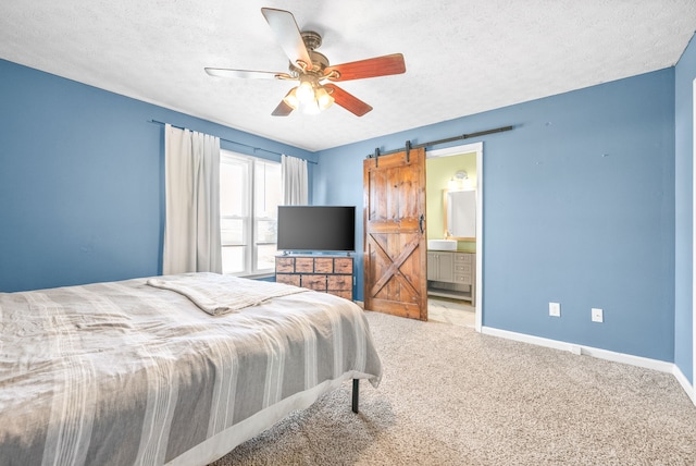 bedroom featuring ceiling fan, a textured ceiling, a barn door, light colored carpet, and connected bathroom