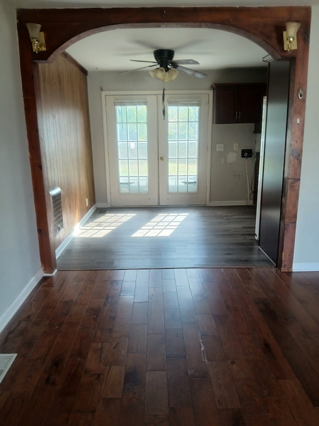 doorway with dark wood-type flooring, ceiling fan, and wooden walls