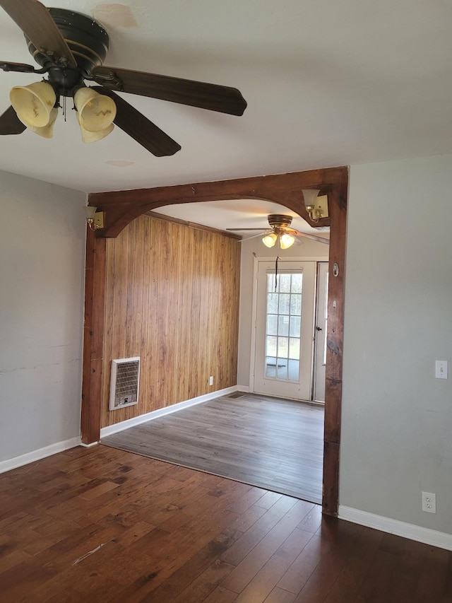 empty room featuring dark wood-type flooring, heating unit, wooden walls, beamed ceiling, and ceiling fan