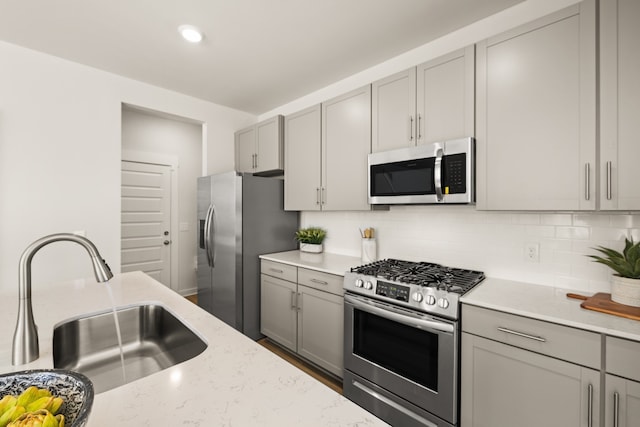 kitchen featuring stainless steel appliances, sink, tasteful backsplash, light stone countertops, and gray cabinets