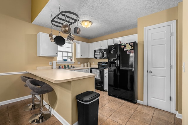 kitchen featuring black appliances, kitchen peninsula, a kitchen bar, light tile patterned floors, and white cabinets