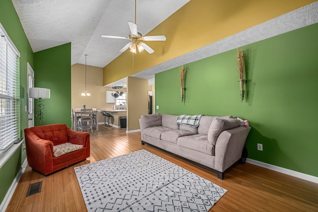 living room featuring wood-type flooring, a textured ceiling, ceiling fan with notable chandelier, and high vaulted ceiling