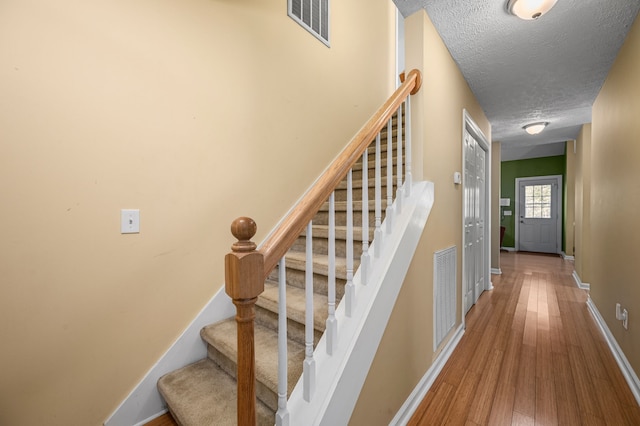 stairway with wood-type flooring and a textured ceiling