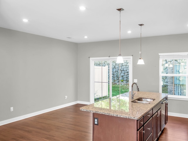 kitchen with dark wood-type flooring, sink, an island with sink, light stone countertops, and pendant lighting