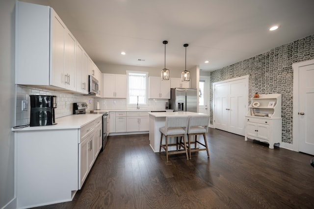 kitchen with white cabinets, dark hardwood / wood-style floors, a kitchen island, pendant lighting, and appliances with stainless steel finishes