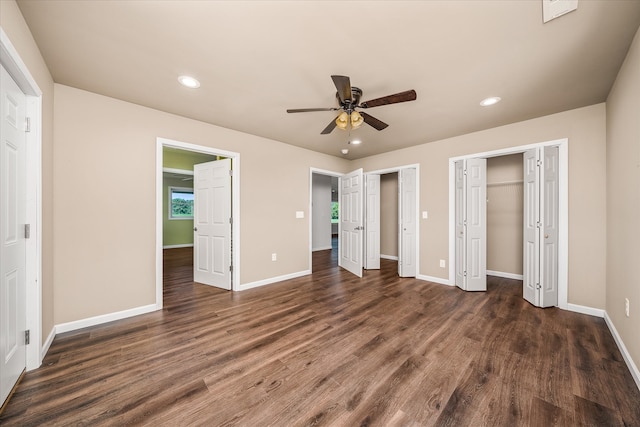 unfurnished bedroom with ceiling fan, dark hardwood / wood-style floors, and multiple closets