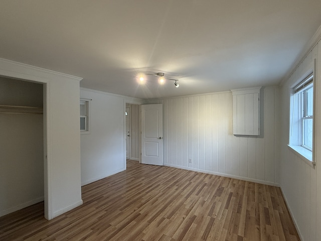 unfurnished bedroom with wood walls, wood-type flooring, a closet, and crown molding