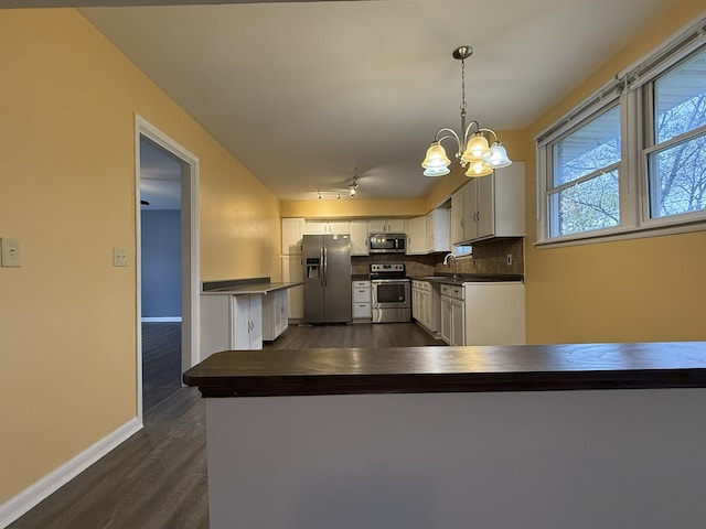 kitchen featuring stainless steel appliances, white cabinetry, tasteful backsplash, decorative light fixtures, and dark wood-type flooring