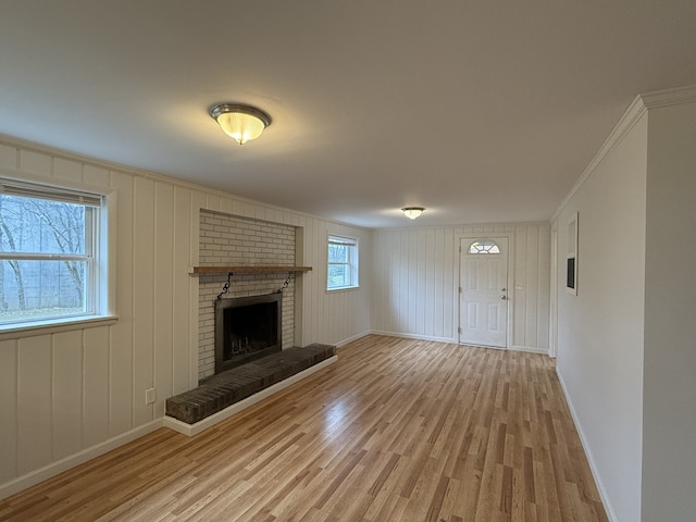 unfurnished living room featuring a brick fireplace, light wood-type flooring, ornamental molding, and a healthy amount of sunlight